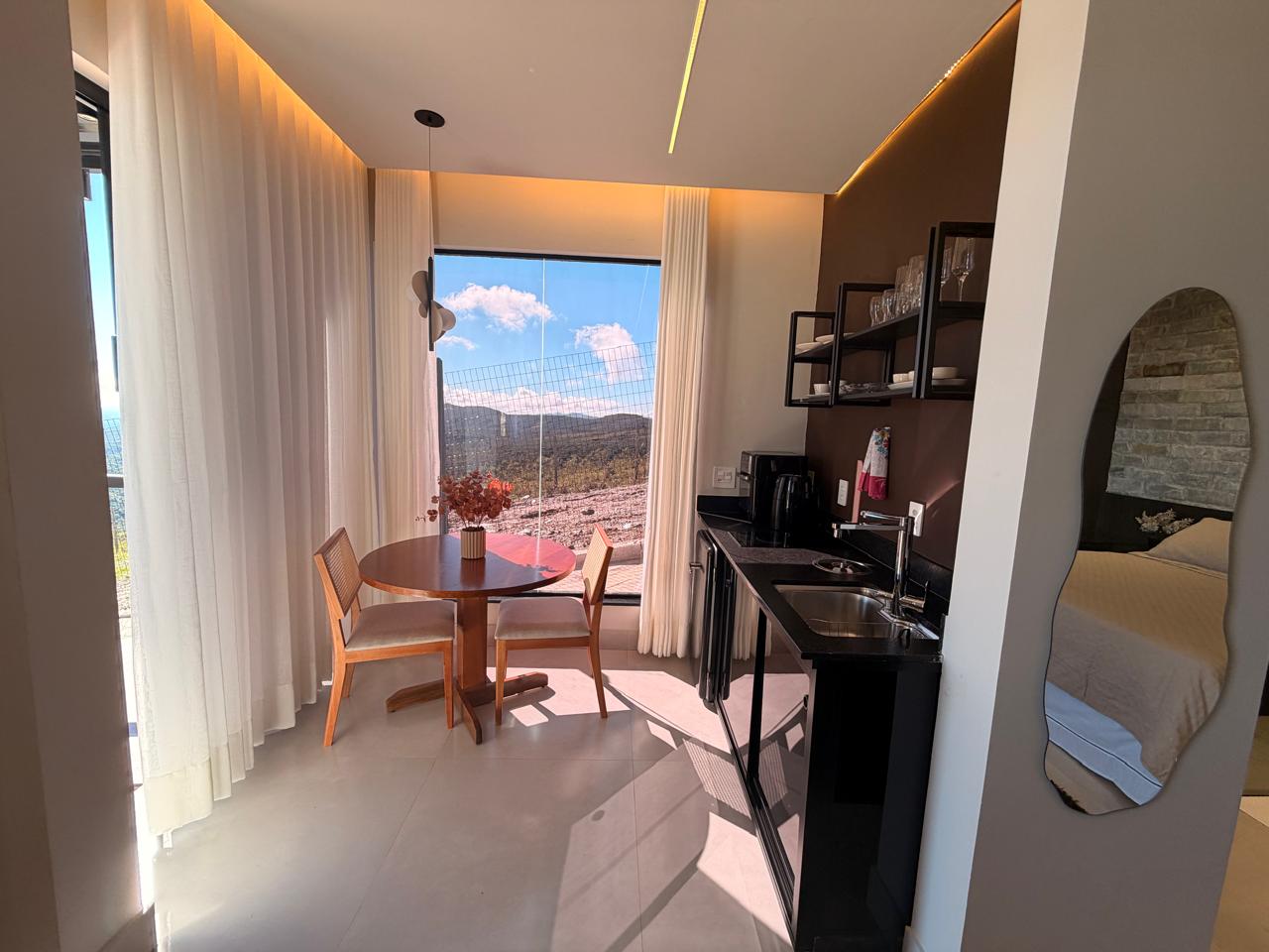 Sala com poltronas e kitchenette diante da janela com vista para a serra no Loft Encanto