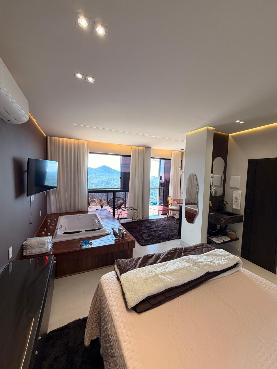 Suíte do Loft Encanto com cama, estar e TV, em Lavras Novas